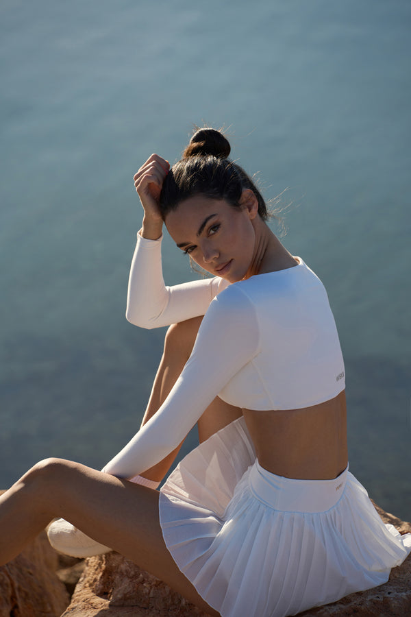 The Ivory White ruched long sleeve sports bra is worn by the model in a side view perspective #1