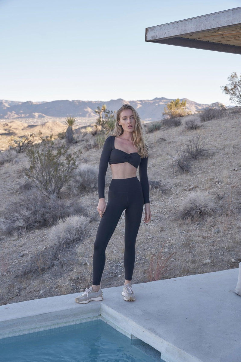 The Black ruched long sleeve sports bra is worn by the model in a front view perspective #2